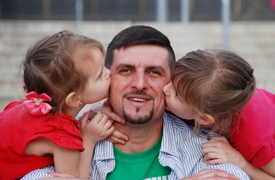 Two young girls kissing their dad on both cheeks